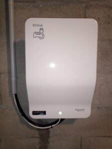 Borne de recharge murale Schneider Electric EVlink blanche sur mur en béton avec voyant lumineux vert allumé.
