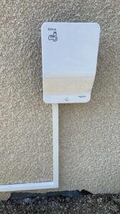 Borne de recharge Schneider Electric EVlink blanche pour véhicule électrique, fixée sur un mur extérieur en crépi beige.