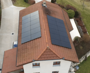 Vue aérienne d'une maison blanche avec panneaux solaires photovoltaïques sur un toit en tuiles terre cuite.