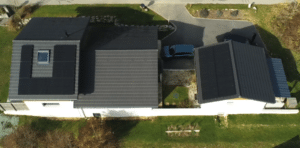 Vue aérienne d'une maison moderne avec panneaux solaires sur le toit et voiture garée dans l'allée ensoleillée.